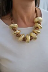 Collar de diseño artesanal compuesto por piezas circulares de metal dorado con acabado mate, intercaladas con nudos de cordón de cuero marrón.