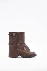 Botas cortas de cuero vegano color marrón, con diseño de caña media y detalle de hebilla metálica en la parte superior. Presentan una estructura con efecto drapeado y suela plana de goma.