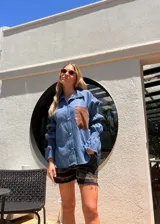 Camisa de jean liviano azul con bolsillo marrón de cuero en el pecho, mangas largas abullonadas con frunces elásticos y cierre frontal con botones.