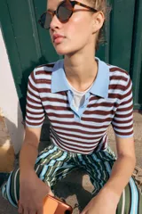 Top de punto de manga corta con diseño a rayas horizontales en tonos marrones y celestes, cuello polo liso en color celeste y cierre frontal con tres botones.