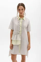 Vestido camisero a rayas con cuello y cartera en tono lima claro, volados frontales y laterales. De calce relajado y mangas cortas. Fabricado en Uruguay.