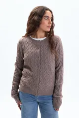 Saco de punto color tostado, con diseño de trenzas verticales en todo el cuerpo y mangas. Tiene cuello redondo y cierre frontal con botones pequeños.