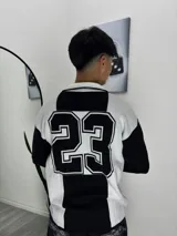 Sweater de tejido de punto con diseño bicolor en blanco y negro, cuello tipo polo y estampado grande del número 23 en la espalda.