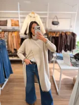 Polera larga de tejido de punto color beige, con cuello alto acanalado y diseño de tajo frontal cruzado. Presenta mangas largas con puños en tono contrastante y corte recto relajado.