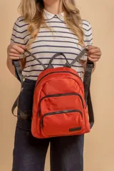 Mochila urbana de diseño funcional en color beige, confeccionada en tela impermeable. Cuenta con un compartimento principal amplio, un bolsillo secundario y un bolsillo frontal, todos con cierre. Incluye asa superior y correas ajustables para los hombros, con detalle de etiqueta de marca en el frente.