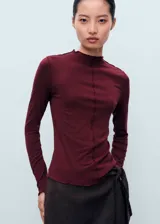 Camiseta bordó de viscosa con elastano, de manga larga y diseño entallado. Cuenta con cuello perkins y terminaciones festoneadas en cuello, puños y ruedo, además de un detalle de costura central frontal.
