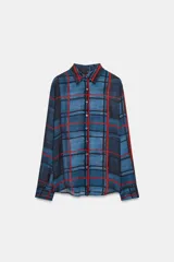 Camisa de manga larga con cuello solapa y cierre frontal con botones. Presenta un diseño de cuadros en tonos azules y rojos sobre un tejido semitransparente.