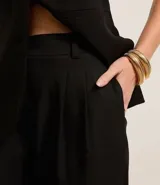 Pantalón de vestir negro, de corte recto, con trabillas en la cintura y pliegues.