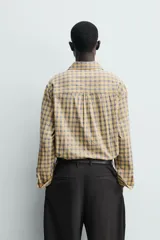 Camisa relaxed fit de algodón con elasticidad, color amarillo y gris a cuadros. Tiene cuello solapa, manga larga con puño abotonado, bajo con aberturas laterales y cierre frontal de botonadura.