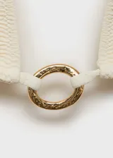 Top de bikini blanco con corte triangular, breteles finos que se atan al cuello y a la espalda, y aro dorado en el centro del busto.