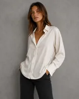 Camisa de satén en tono beige, de corte clásico y holgado, con cuello camisero, cierre frontal de botones y puños anchos.