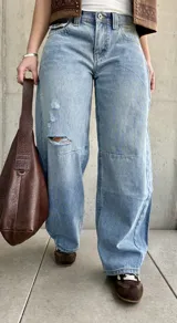 Jean de denim celeste de corte barrel, tiro bajo, con roturas y detalles desgastados en la rodilla.