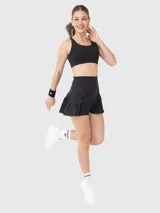 Falda deportiva tipo skort color negro, con cintura alta y diseño de pliegues en el ruedo. Incluye short integrado con bolsillo lateral.
