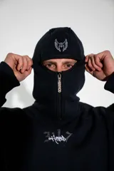 Canguro negro con capucha, cierre frontal parcial y bolsillo tipo canguro. Presenta un estampado gráfico pequeño en el centro del pecho.