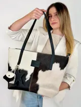 Cartera tote de cuero con pelo vacuno en tonos blanco y negro, con asas largas de hombro, parche frontal con logo y charms colgantes en forma de estrella y mini monedero.