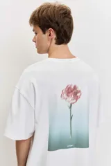 Remera blanca de manga corta, corte oversize, con estampa en la espalda de una flor sobre fondo difuminado verde y blanco.