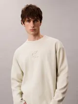 Sweater de punto color beige con cuello redondo, mangas largas y corte regular. Cuenta con el logo distintivo de Calvin Klein bordado en relieve al tono en el pecho.