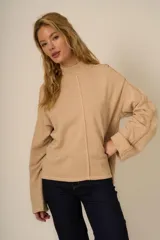 Buzo color beige de cuello alto con mangas acampanadas y detalles de costura.