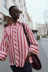 Camisa de cuello solapa con estampado de rayas verticales en tonos rojos, rosas y blancos. Presenta cierre frontal con botones y mangas tres cuartos con puño vuelto.