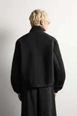 Cazadora de corte boxy fit en tejido compacto con elasticidad, color negro. Presenta cuello subido, manga larga con puños elásticos, bolsillos frontales de vivo y cierre frontal con cremallera oculta por solapa con botones a presión.
