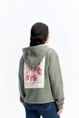 Canguro de algodón color beige con capucha amplia y corte relajado. Presenta un estampado rectangular en la espalda con motivos florales en tonos azules y el texto 'Harmony of Bloom'.