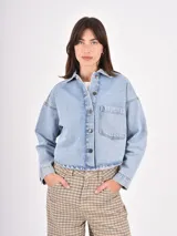 Sobrecamisa de denim en tono azul claro, con corte oversize, cuello clásico, cierre frontal con botones metálicos y un bolsillo de parche en el pecho.