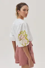 Camisa blanca de mezcla lino-algodón, con corte recto y mangas clásicas. Presenta un bordado floral en el hombro con distintas técnicas y canutillos.