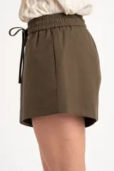 Short verde militar de lino y poliéster, de tiro medio con cintura elástica fruncida y cordón ajustable delantero. Cuenta con bolsillos laterales.