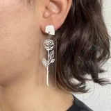 Aros colgantes largos de acrílico transparente con diseño de rosa grabada en blanco y pieza superior cuadrada de color blanco.