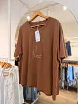 Remerón oversize color marrón, confeccionado en algodón, con cuello redondo, mangas cortas y estampa frontal minimalista en línea blanca que representa una figura humana junto a un perro.