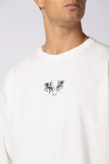 Remera de corte oversize color blanco hueso, con cuello redondo y estampa pequeña centrada en el pecho que presenta dos figuras de caballos alados.