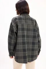 Camisa de corte oversize con estampado de cuadros en tonos marrones y negros. Presenta cuello clásico, cierre frontal de botones metálicos y dos bolsillos con solapa en el pecho.