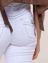 Pantalón jean de tiro medio y calce bootcut color blanco, confeccionado en denim elastizado con visibles pespuntes decorativos a contraste en pretina, bolsillos frontales y traseros. Presenta bolsillos posteriores con botón metálico y cierre frontal con cremallera y botón.