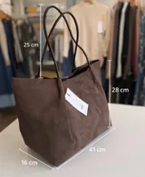 Bolso tipo shopper de material sintético con acabado efecto gamuza en color marrón, con asas largas para llevar al hombro. Incluye un neceser interno de material brillante a tono con cierre metálico.