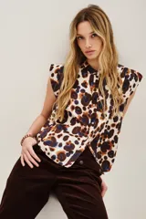 Camisa sin mangas con cuello camisero y botones frontales, confeccionada en tela estampada con patrón animal print en tonos blanco, marrón y azul oscuro.