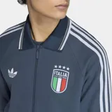 Campera deportiva Adidas de la selección de Italia, color azul con diseño retro. Presenta cuello tipo polo, cierre frontal completo, bolsillos laterales y las icónicas tres tiras de la marca en las mangas. Incluye el logo del Trifolio y el escudo de la Federación Italiana de Fútbol en el pecho.