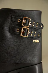 Bota de caña corta negra confeccionada en cuero, con detalle de botamanga y hebillas doradas.