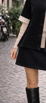 Capa de terciopelo negro con corte de chaqueta, cuello alto y mangas cortas. Presenta detalles de puntilla de algodón en el cuello y en los bordes de las mangas, con cierre frontal de botones.