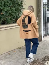 Campera tipo hoodie de corderito color camel, con diseño de collage abstracto en la espalda que combina texturas y estampados geométricos. Posee capucha y corte holgado.