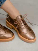Zapato acordonado estilo Oxford de cuero vacuno en color bronce metalizado, con diseño brogue y suela de goma con plataforma.