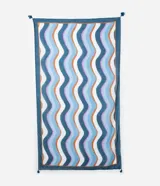 Pareo rectangular de chiffon con estampado de ondas en tonos de azul, blanco, naranja y lila. Tiene borde azul con borlas en las esquinas.