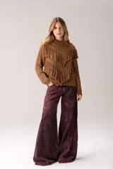 Sweater de punto color crema con cuello medio alto y silueta relajada. Presenta un diseño frontal con líneas en V decoradas con flecos largos de color marrón aplicados a mano.