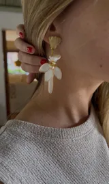 Aros colgantes hechos a mano con diseño floral, con una pieza superior dorada texturada, perlas de río y pétalos esmaltados en blanco con bordes dorados.