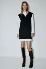 Vestido corto que combina una camisa blanca de manga larga con cuello solapa y botones frontales, con un chaleco de tejido negro de punto con escote en V.