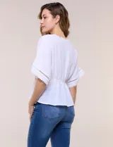 Blusa blanca de poliéster con textura crepada, escote en V con detalles de puntilla, mangas cortas amplias estilo kimono y diseño semi entallado bajo el busto con faldón suelto.