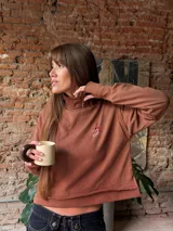 Buzo de algodón rústico color crema, con cuello redondo, corte boxy y costuras externas visibles. Presenta puños con abertura para el pulgar y un bordado pequeño en el pecho.
