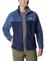 Campera polar Columbia con cierre frontal completo, cuello alto y bolsillos laterales con cierre. Presenta un diseño de bloques de color en dos tonos de azul y el logo de la marca bordado en el pecho.