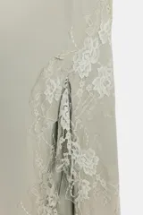Vestido largo lencero de tejido fluido en color gris verdoso, con escote en V, tirantes finos y detalles de encaje a tono en el bajo y los laterales, además de una abertura frontal.