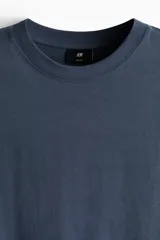 Remera de algodón de peso medio, color azul, con cuello redondo ribeteado, hombros caídos y corte relajado.