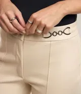 Pantalón legging color beige con frente de poliuretano que imita cuero y parte trasera de punto roma. Presenta detalle de cadena metálica en la cintura y cierre frontal.